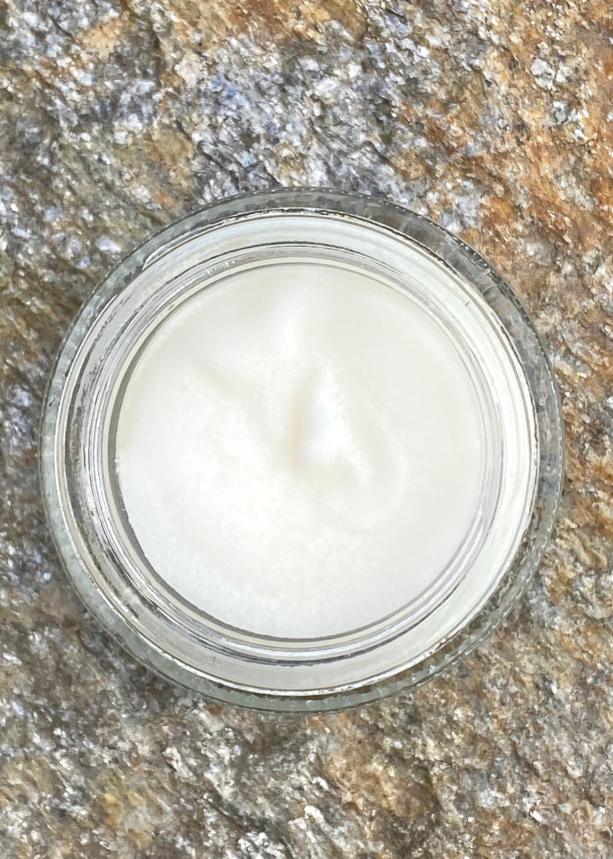 InspireByMK all-natural balm in clear glass jar with creamy white texture displayed on rustic stone surface, handcrafted moisturizing balm with pure essential oils and organic ingredients