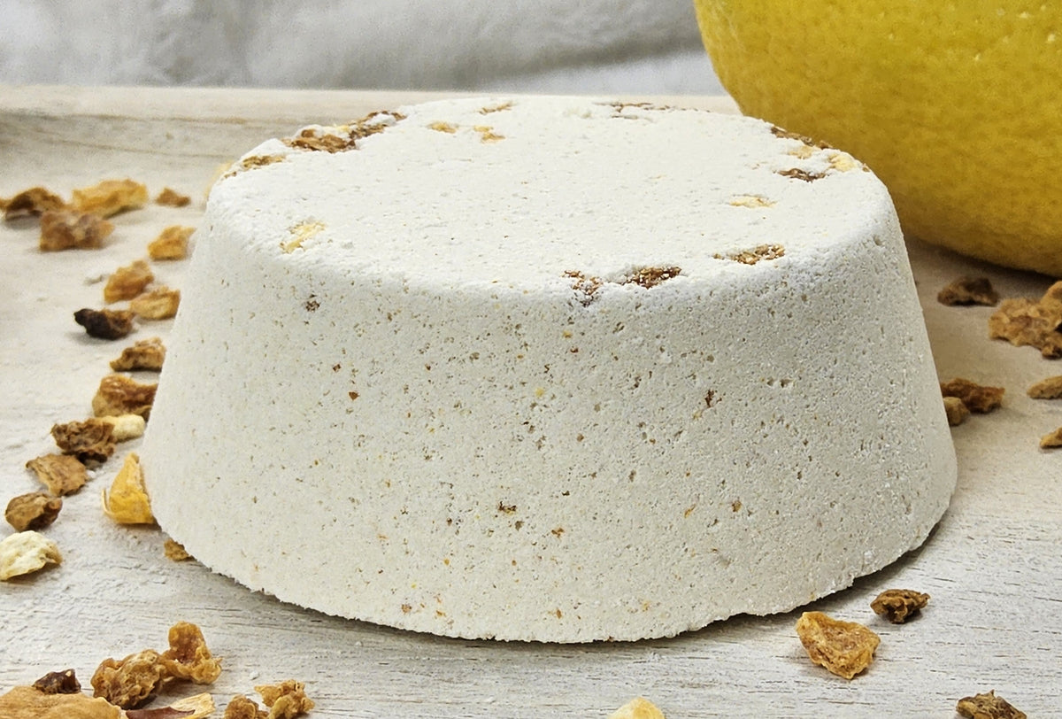 InspireByMK Citrus shower steamer handcrafted dome with cream base and golden dried botanicals, surrounded by fresh lemon, lime, and grapefruit fruits showing lemon, grapefruit, orange, and lime essential oil blend with rosemary hydrosol