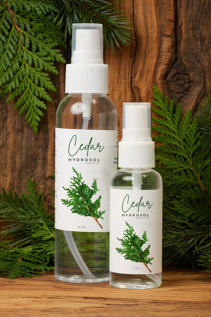 Cedar Hydrosol 4oz and 2oz spray bottles displayed with fresh cedar branches on rustic wood. All natural organic cedar hydrosol smudging spray, room spray, facial mist and hydrating face toner. Pure steam-distilled cedar hydrosol for calming, grounding and positive energy.