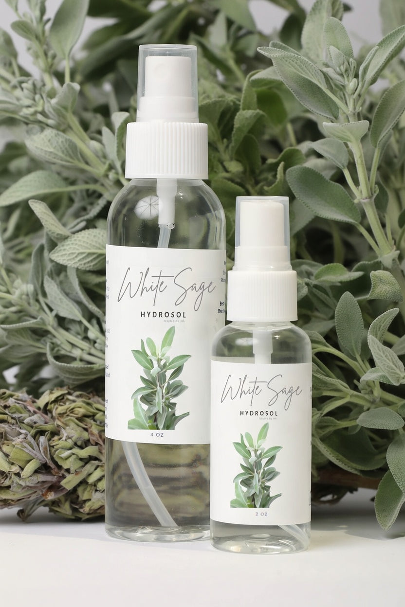White Sage Hydrosol 4oz and 2oz spray bottles displayed with fresh white sage and dried sage bundle. All natural organic white sage hydrosol smudging spray, purifying facial mist, and grounding room spray. Pure steam-distilled white sage hydrosol for energy cleansing and spiritual aromatherapy.
