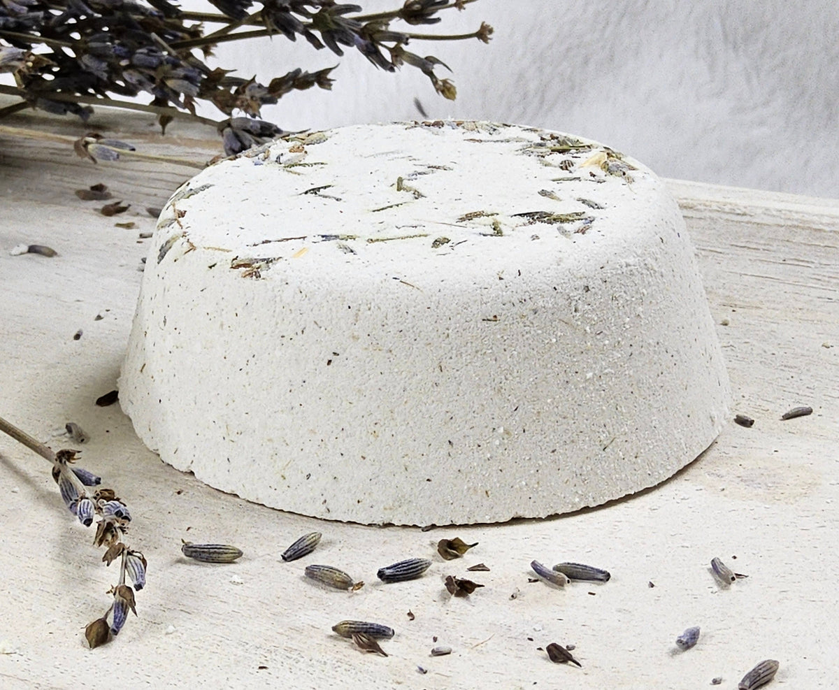 InspireByMK Lavender shower steamer handcrafted dome with cream base and gray-green dried lavender leaves and stems, surrounded by fresh lavender showing pure lavender essential oil with lavender hydrosol for sleep support and relaxation