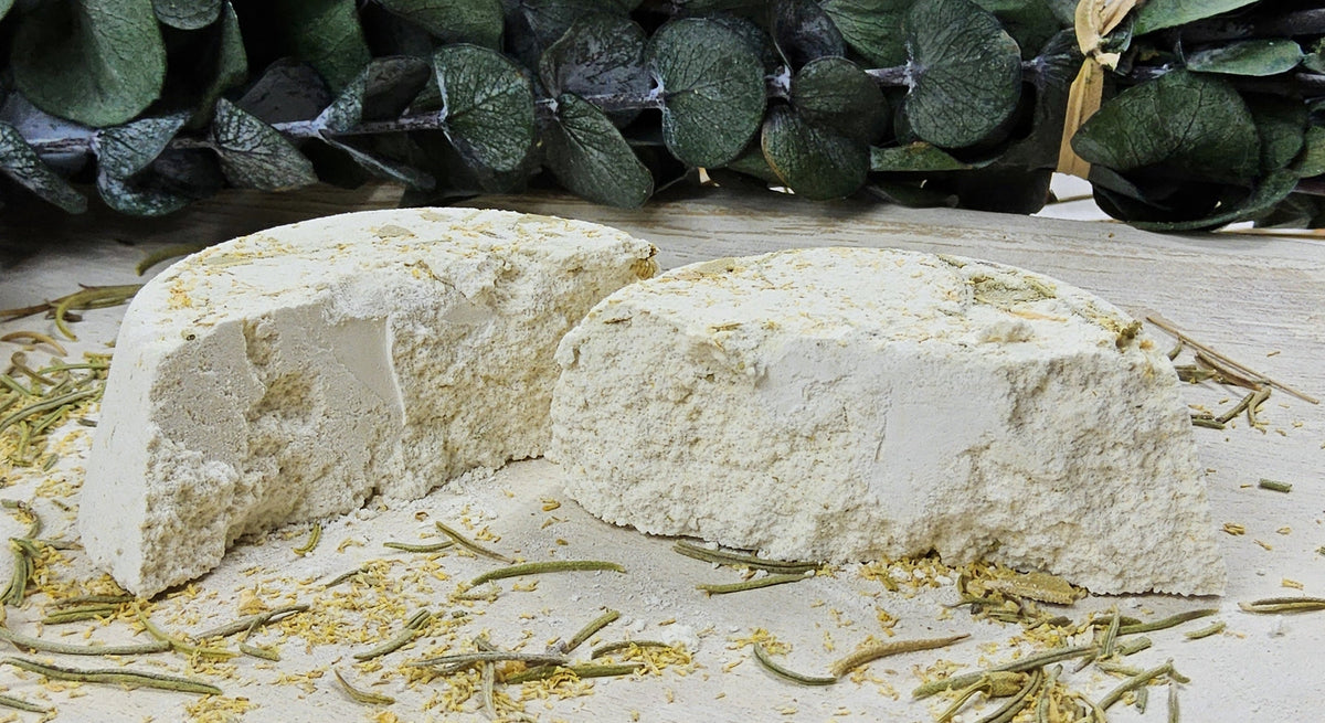 InspireByMK Revive shower steamer sliced in half revealing all-natural golden dried botanical ingredients throughout, demonstrating handcrafted quality with lemon, clove, eucalyptus, rosemary essential oils and rosemary hydrosol, surrounded by fresh citrus and herb styling