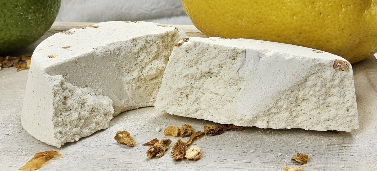 InspireByMK Citrus shower steamer sliced in half revealing all-natural ingredients including golden dried botanicals throughout, demonstrating handcrafted quality with lemon, grapefruit, orange, lime essential oils and rosemary hydrosol, surrounded by fresh citrus and dried peel styling
