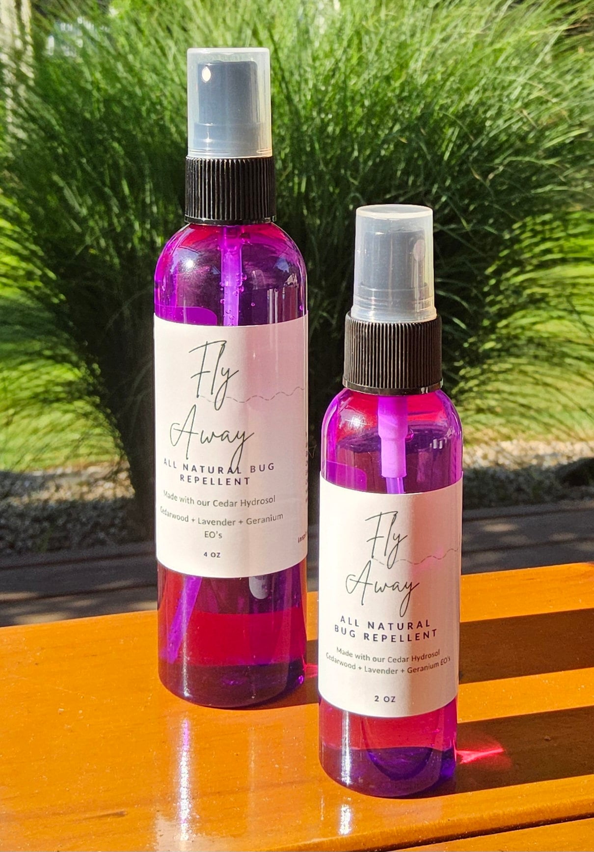 InspireByMK Fly Away Cedar All Natural Bug Repellent duo featuring 4 oz and 2 oz purple glass spray bottles with black caps, made with cedar hydrosol, cedarwood, lavender, and geranium essential oils, DEET-free kid and pet-safe insect repellent displayed with fresh cedar foliage