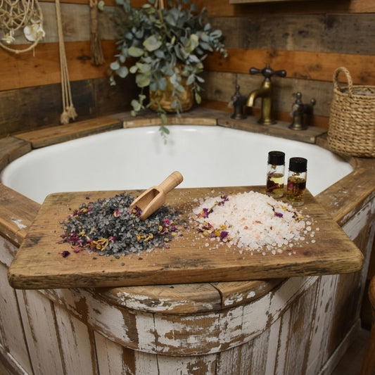 InspireByMK rustic spa bathroom display showing floral bath salts lava and epsom blends with dried rose petals, jasmine, lavender, and chamomile on wooden tray across whitewashed bathtub, paired with floral hydrosol bottles, wooden scoop, and natural botanical decor for aromatherapy bathing