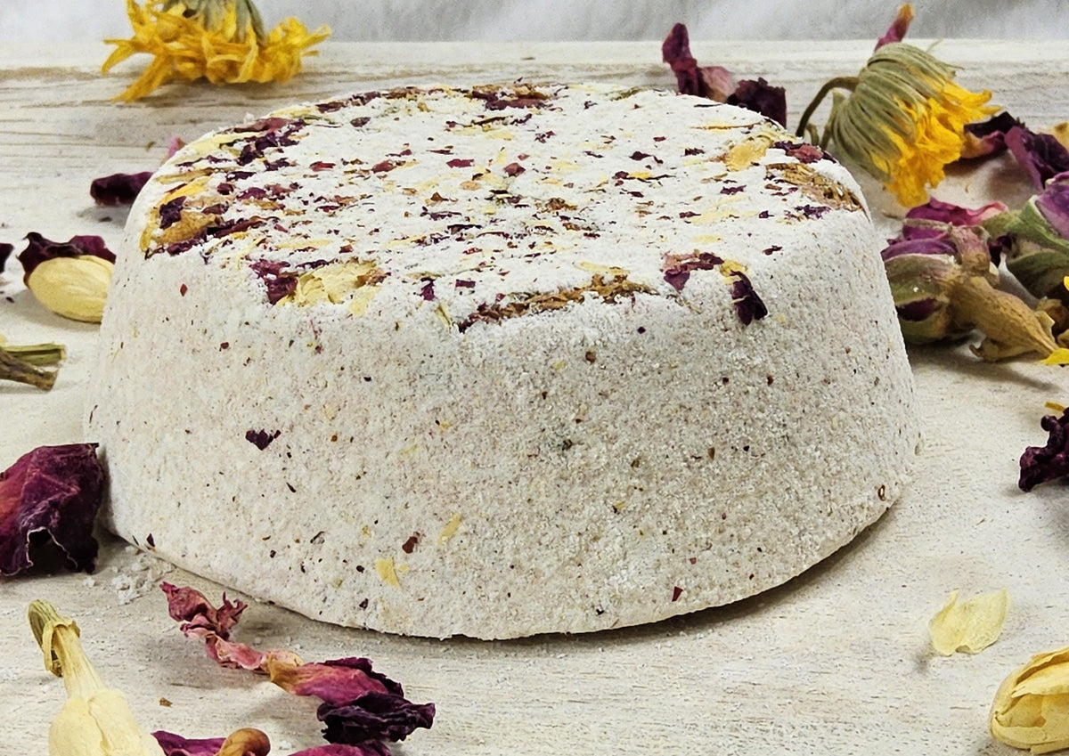 InspireByMK Restore shower steamer handcrafted dome with cream base and dark purple and golden dried botanicals, surrounded by deep red roses showing sandalwood, patchouli, bergamot essential oil blend with rose hydrosol for grounding aromatherapy