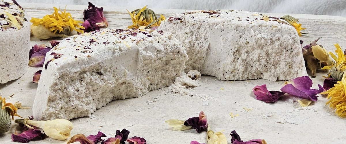 InspireByMK Restore shower steamer sliced in half revealing all-natural purple and golden dried botanical ingredients throughout, demonstrating handcrafted quality with sandalwood, patchouli, bergamot essential oils and rose hydrosol, surrounded by deep red roses