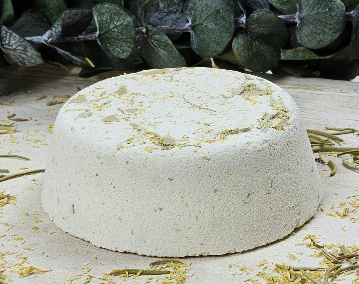 InspireByMK Revive shower steamer handcrafted dome with cream base and golden dried botanicals, surrounded by fresh lemon and herbs showing lemon, clove, eucalyptus, rosemary essential oil blend with rosemary hydrosol for energy and focus