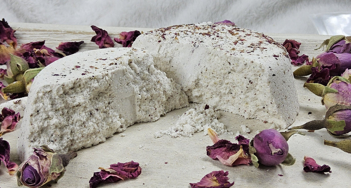 InspireByMK Rose shower steamer sliced in half revealing all-natural dark purple dried rose petals throughout, demonstrating handcrafted quality with pure rose essential oil and rose hydrosol, surrounded by fresh red roses for luxurious spa aromatherapy