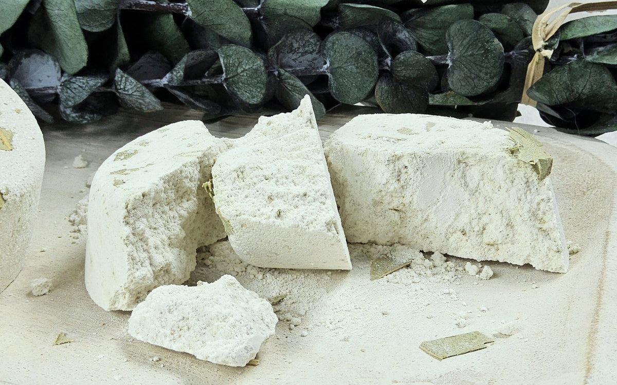 InspireByMK Eucalyptus shower steamer sliced in half revealing all-natural dried eucalyptus leaves throughout, demonstrating handcrafted quality with pure eucalyptus essential oil and eucalyptus hydrosol, surrounded by fresh eucalyptus botanical styling